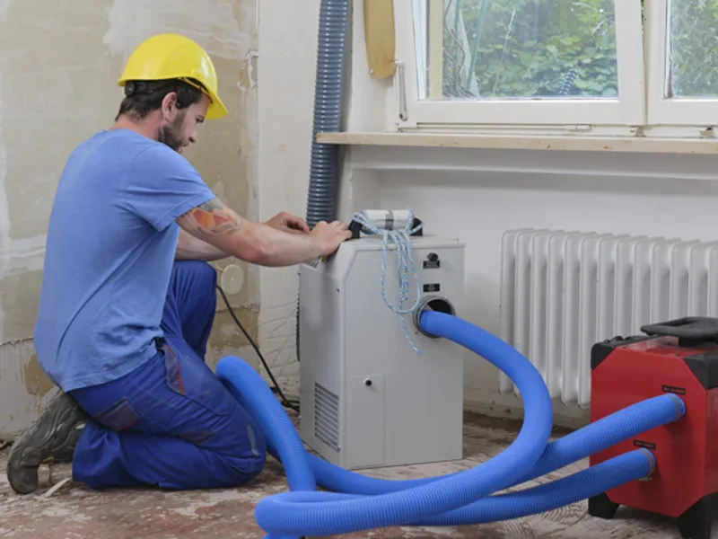Technician adjusting a dehumidifier while drying out a water-damaged room