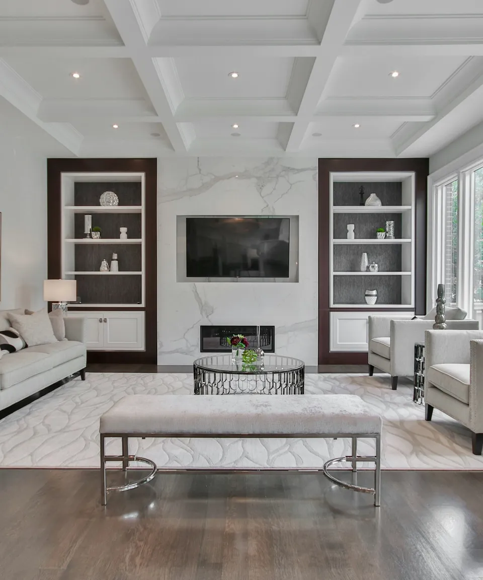 Elegant living room with a coffered ceiling, marble fireplace wall, and dark built-in shelving