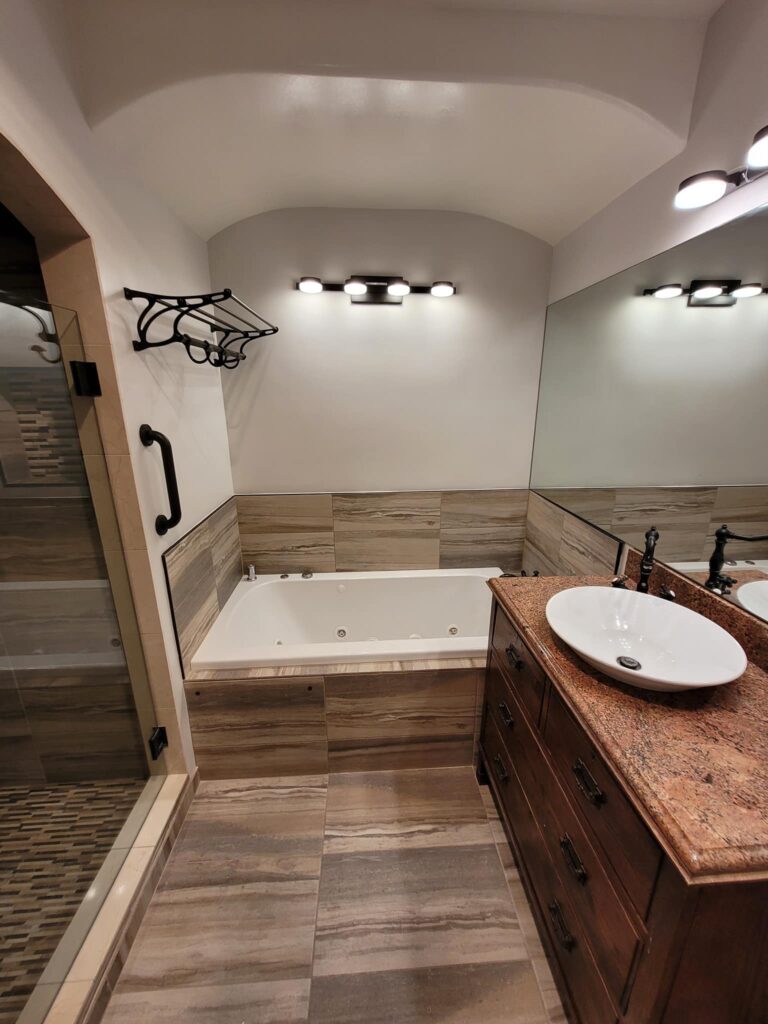 Remodeled bathroom with a tiled soaking tub, wood vanity, and granite top