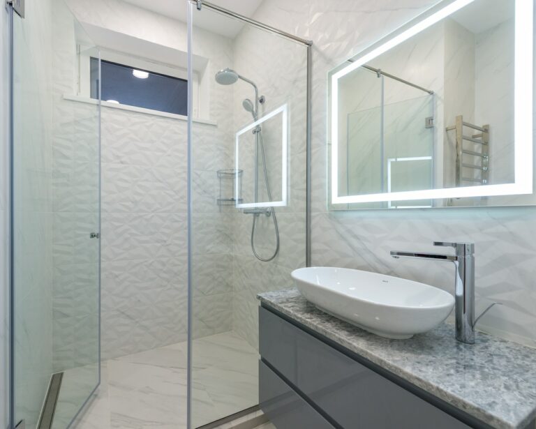 Glass walk-in shower beside a floating vanity with a backlit mirror