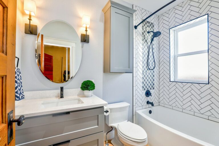 Bathroom with a gray vanity, round mirror, and white herringbone shower tile